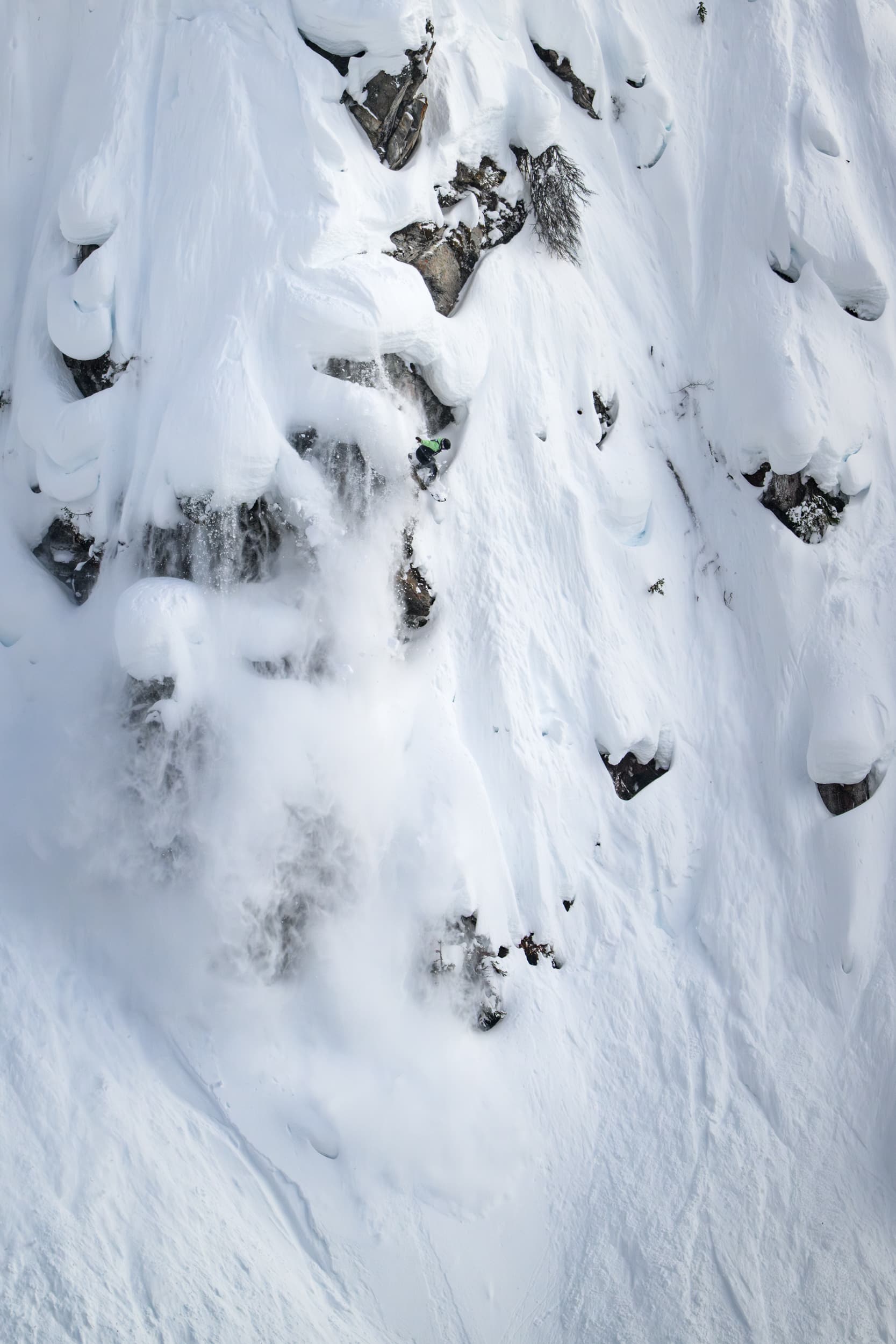 A skier makes their way down a steep, snow-covered mountain slope, surrounded by rocks and fresh powder snow.