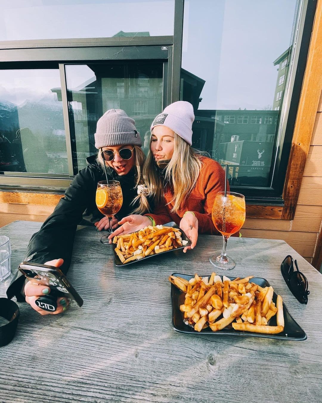 two girls sipping drinks and eating poutine
