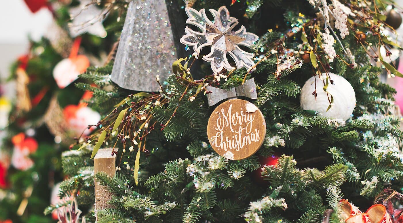 Close-up of a decorated Christmas tree with a "Merry Christmas" ornament, snowflake, and various festive decorations.