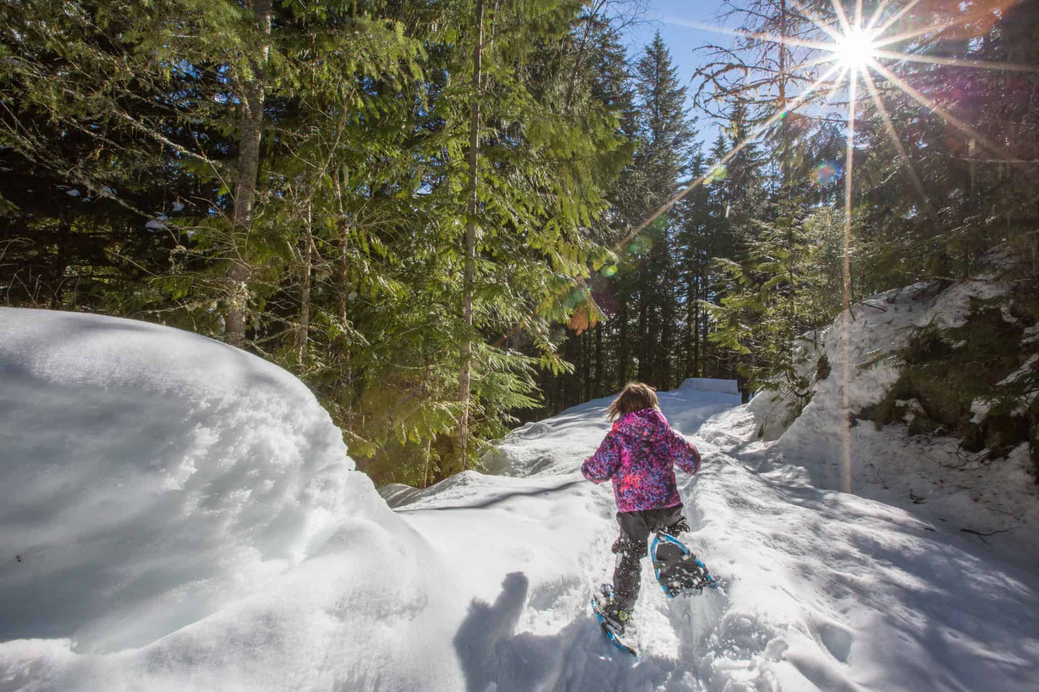 little girl running with snowshoes on forested trail