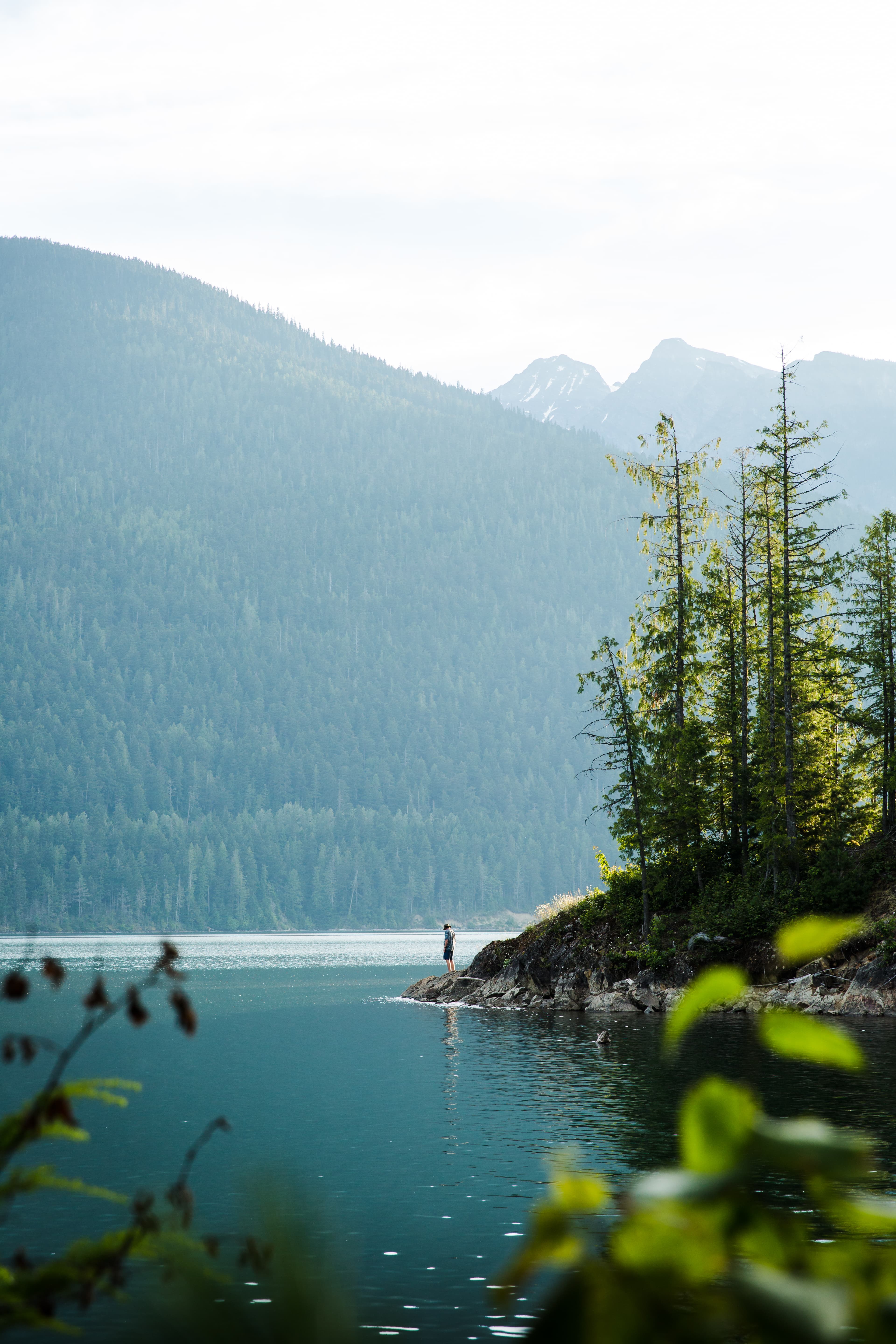 man standing on inlet point with mountains towering above