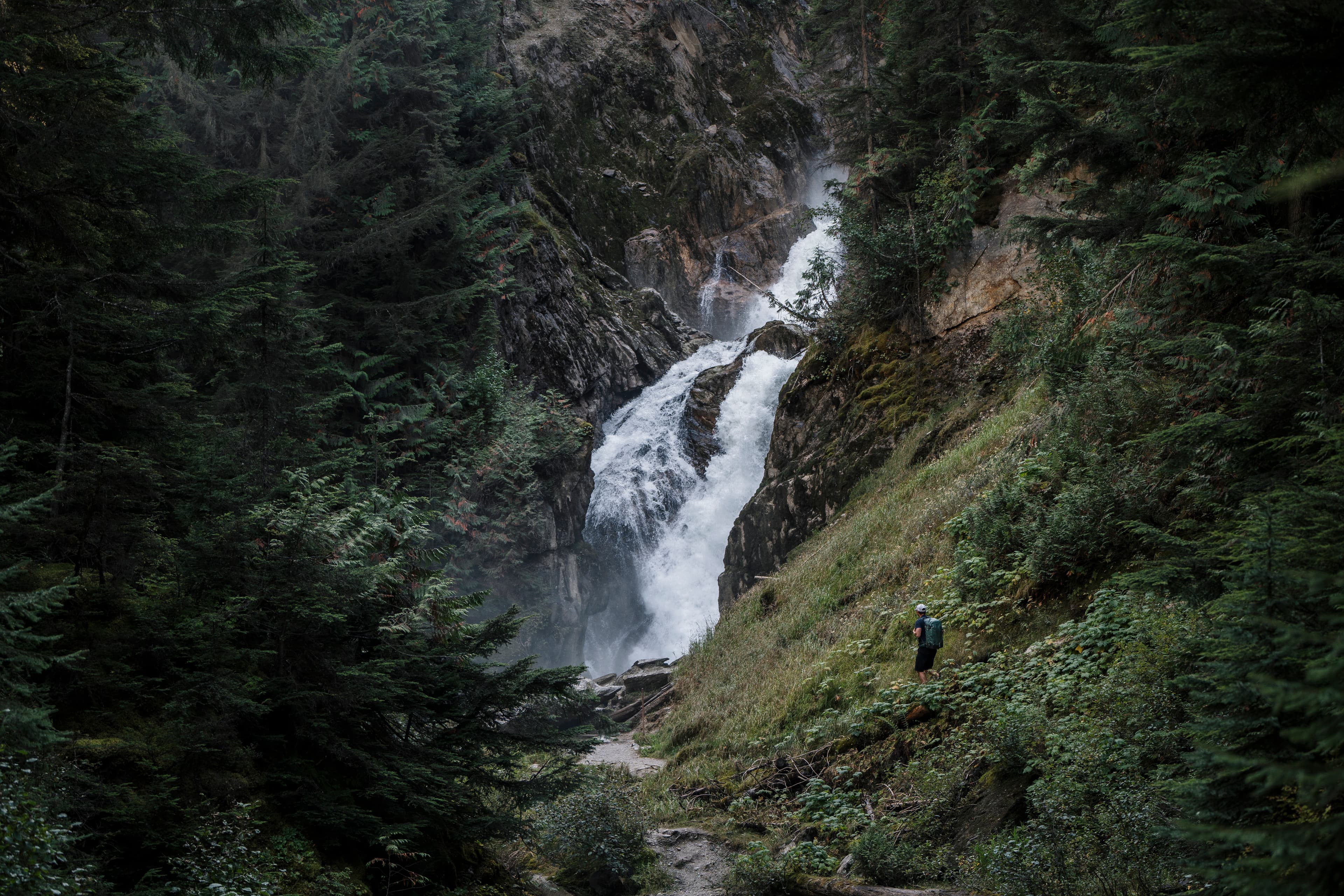 individual hiker walking towards massive waterfall in lush forest