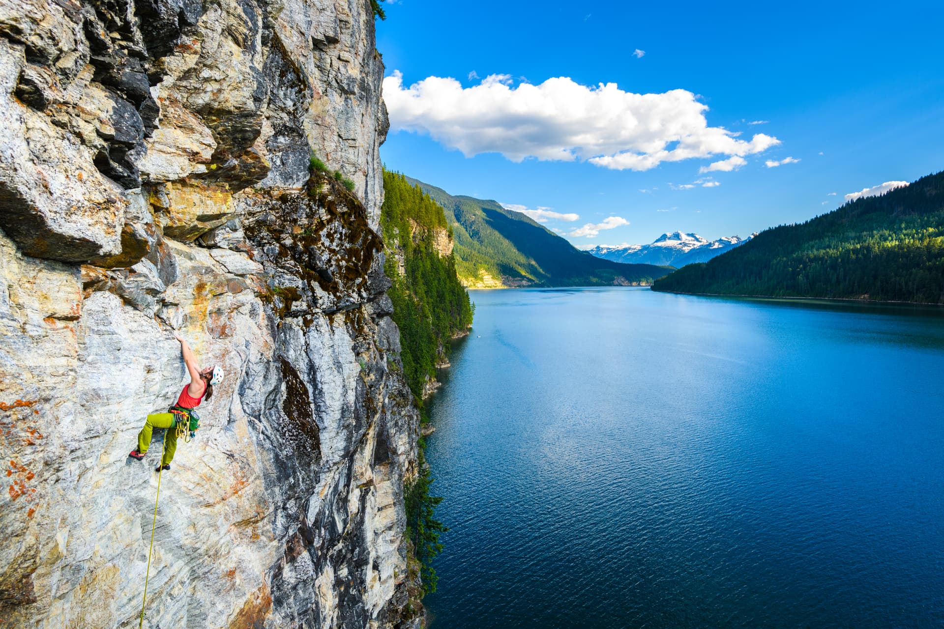 single climber on rock face above lake
