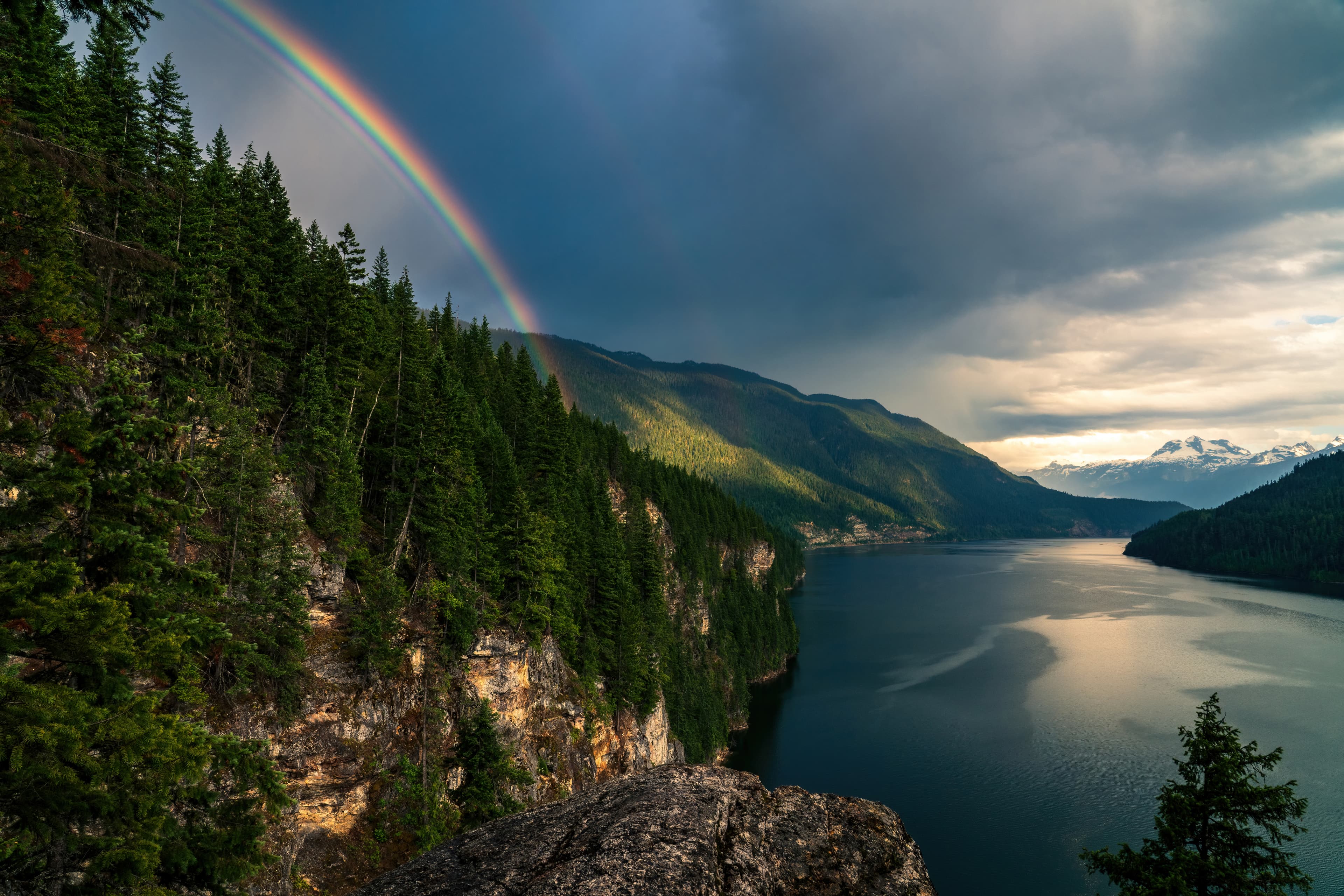 A rainbow disappears behind a mountain beside Lake Revelstoke