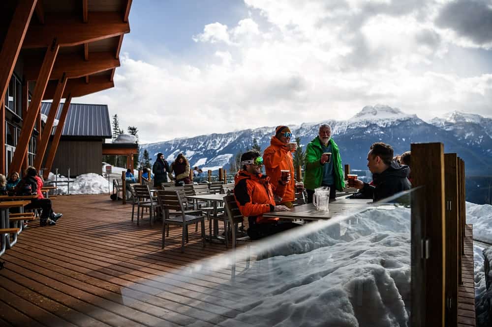 A group of skiers raise a glass of Mt Begbie beer towards Mt Begbie itself, at the Revelation Lodge at Revelstoke Mountain Resort.