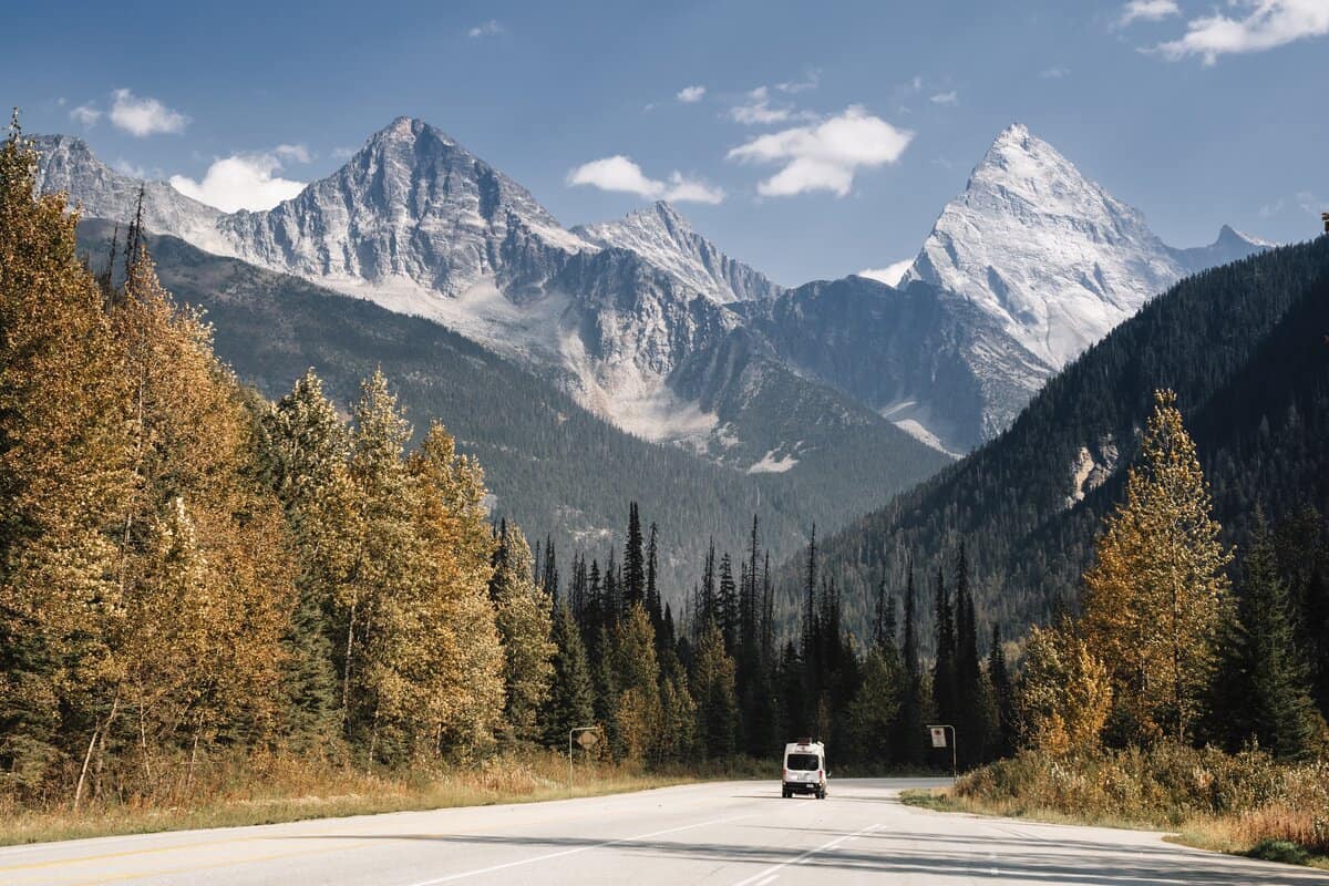 van driving on highway with view of towering mountains and fall colours